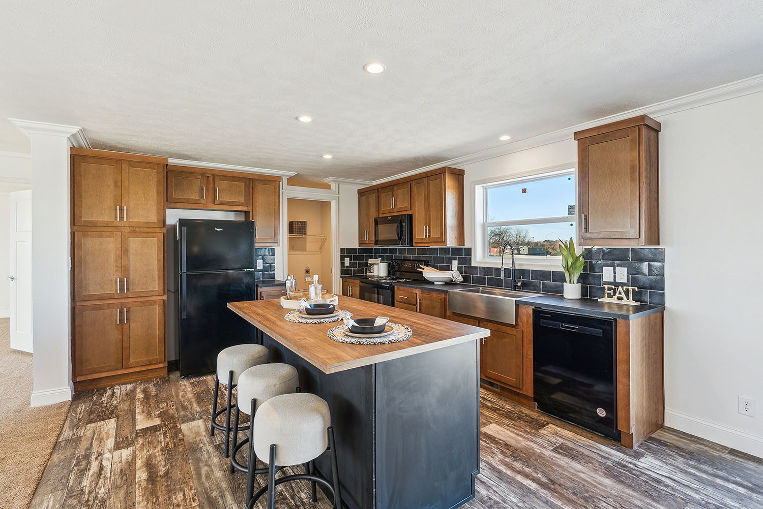 The kitchen with brown and black cabinets. There are three bar stools at an island.
