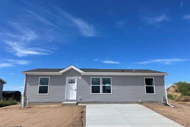 Gray house with a white front door. There is a cement driveway. It is blue sky above the house.